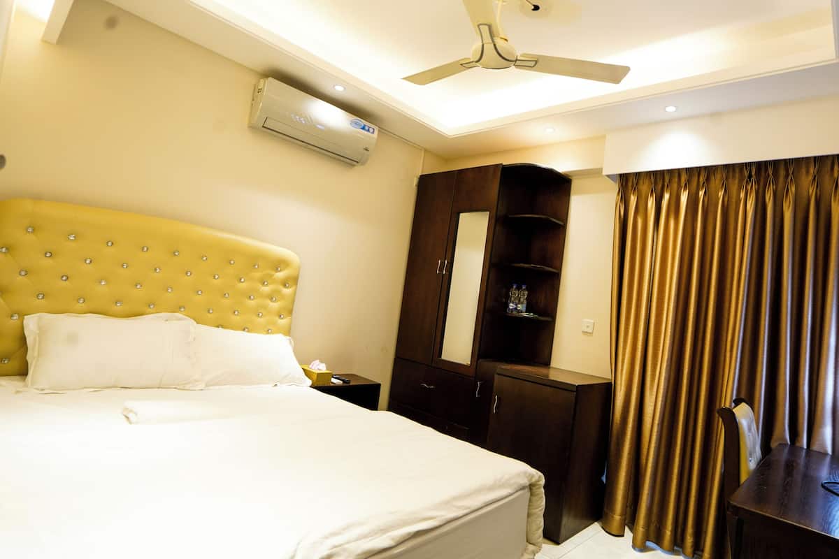 A hotel room with a large bed, a wardrobe, a desk with a lamp, and a ceiling fan.