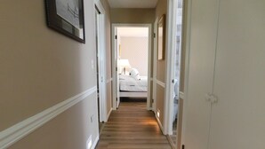 Ein Flur mit Holzboden, weißen Wänden und Türen zu einem Schlafzimmer mit Bett und Nachttisch.