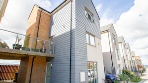 En modern bostadsbyggnad med en grå fasadbeklädnad, en sektion i tegel och en liten balkong med planterade blommor i krukor.