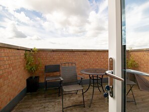 Un patio con un muro in mattoni, un tavolo rotondo, due sedie e una porta in vetro.
