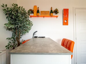 Cucina con piano di lavoro in cemento, lavello incassato e ripiano con bottiglie e un cartello.
