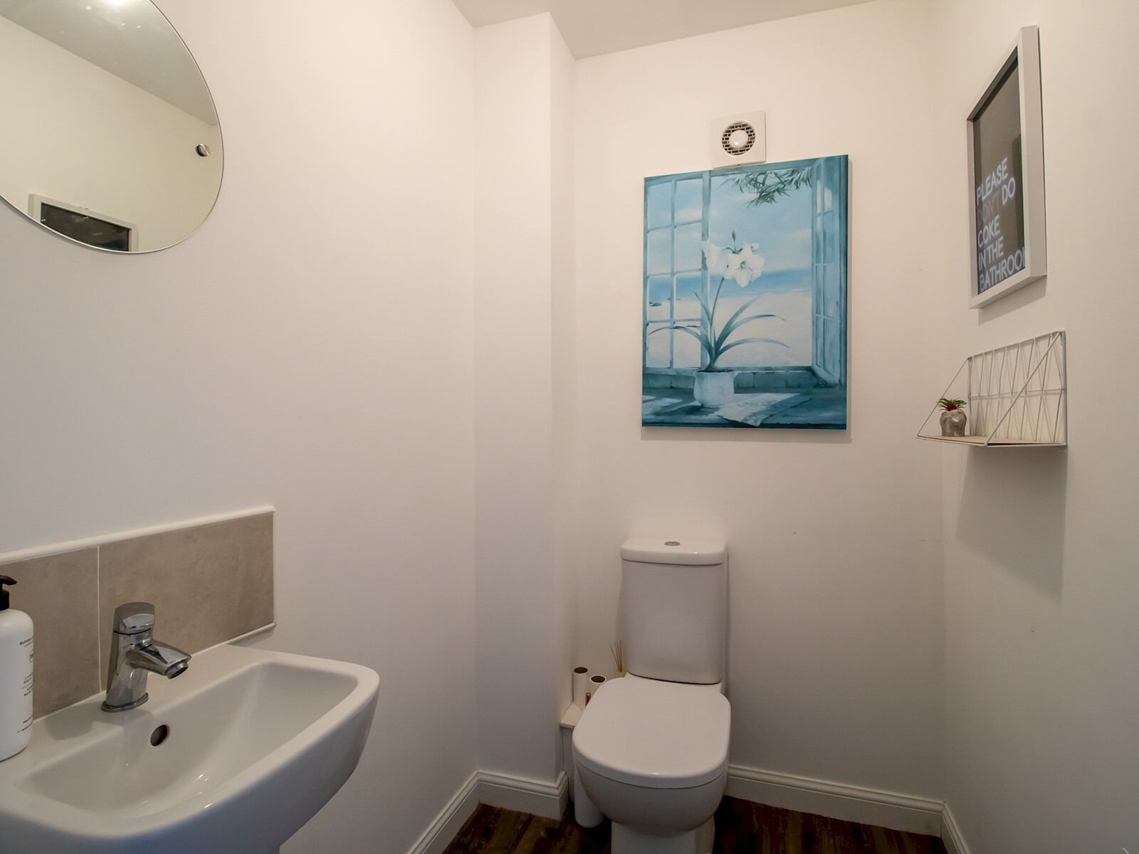 A bathroom with a white sink, toilet, and a painting of a window with plants.