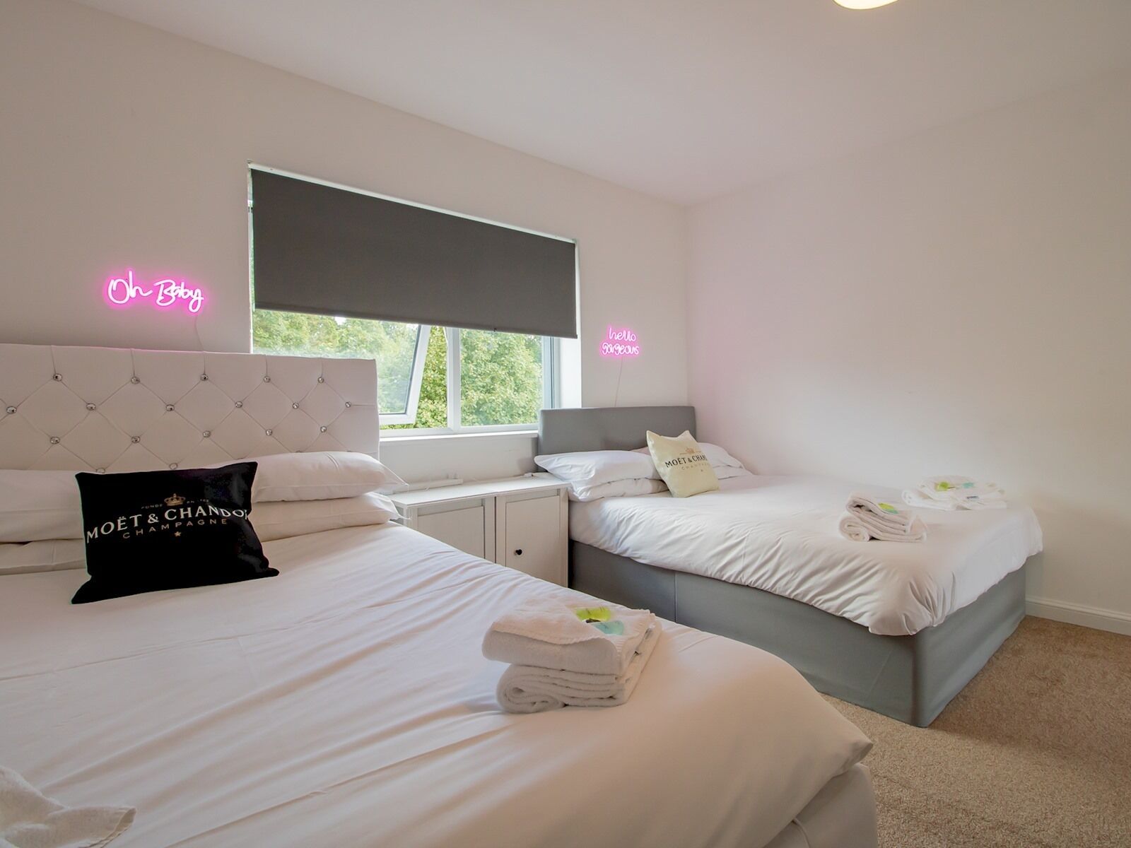 A hotel room with two beds, a window with a view, and neon signs on the walls.