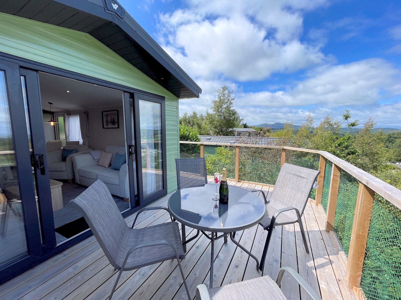 Um terraço com porta de vidro que dá para uma sala de estar, mesa redonda com cadeiras e vista panorâmica da paisagem.