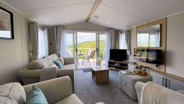 Ein gemütliches Wohnzimmer mit einer Sofagarnitur, einem Couchtisch und einem Flachbildfernseher. Ein Balkon mit Tisch und Stühlen bietet einen reizvollen Blick ins Grüne.