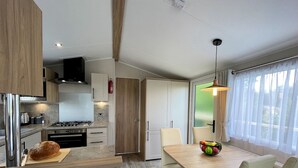 Eine moderne Küche mit Herd, Backofen und Kühlschrank. Es gibt einen Essbereich mit Tisch und Stühlen sowie ein Fenster mit Vorhängen.