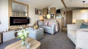 Ein modernes Wohnzimmer mit Flachbildfernseher, einer Couch, einem Couchtisch mit Blumen und einer Küchenzeile im Hintergrund.