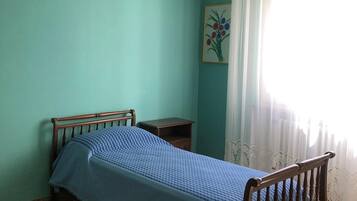 A bedroom with a single bed, a nightstand, a hanging light fixture, and a window with curtains.