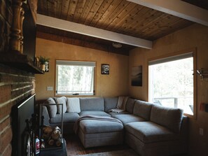 A cozy living room with a sectional sofa, a fireplace, and a large window providing natural light. - Pike National Forest Cabin with Mountain Views, Deck & Wood Fireplace (Woodland Park)