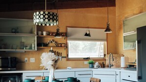Una cocina con armarios de madera, una mesa de comedor con sillas, una lámpara colgante y una ventana con persianas.