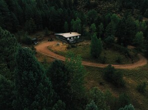 A remote cabin surrounded by dense forest, with a dirt path leading to it. - Pike National Forest Cabin with Mountain Views, Deck & Wood Fireplace (Woodland Park)