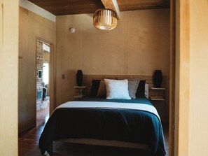 A bedroom with a bed, wooden headboard, and a hanging light fixture.