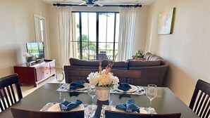 A dining area with a table set for four, a sofa in the background, and a TV on a stand to the left.