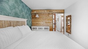 Ein Schlafzimmer mit einem großen Bett, einem Holzkopfstück, einer Wand mit tropischem Blattmuster, einer Holzbank und einem Spiegel mit rustikalem Rahmen.