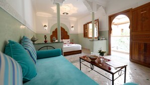 A room with a teal sofa, a bed with a wooden headboard, a small table with a vase, and a view of the outside. - Marrakech (Marrakech)