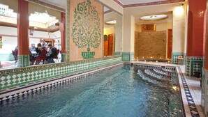 A swimming pool with intricate tile patterns, a seating area with people, and a large decorative wall. - Marrakech (Marrakech)