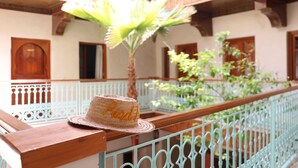 A straw hat on a balcony railing with a view of a building's exterior, including a palm tree and a white fence. - Marrakech (Marrakech)