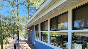 A covered deck with a railing, large windows, and a view of trees.