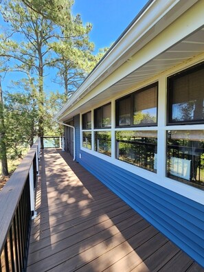 Eine überdachte Veranda mit Holzdeck, großen Fenstern und einem Geländer.