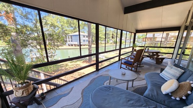A covered outdoor seating area with a view of a lake and trees, a sofa, and a small table.