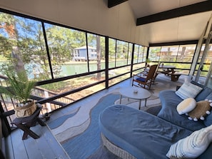 A covered outdoor seating area with a view of a lake and trees, a sofa, and a small table.