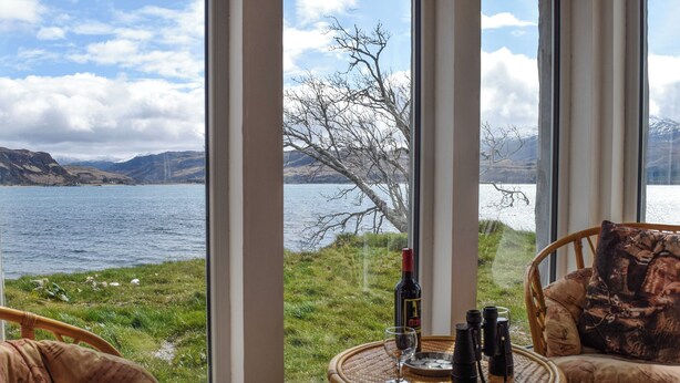 A room with a view of a lake and mountains, wicker furniture, and a bottle of wine on a table. - The House on the Point - UK43807 (Kylerhea)