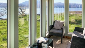 A room with large windows, wicker furniture, and a view of a lake and mountains. - The House on the Point - UK43807 (Kylerhea)