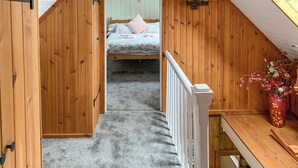 A narrow, wooden-paneled room with a sloped ceiling, a bed with floral bedding, a white railing, and a vase with flowers on a table. - The House on the Point - UK43807 (Kylerhea)
