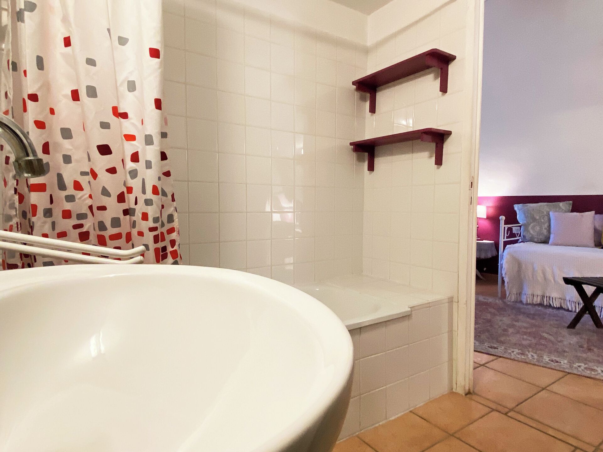 A bathroom with a white sink, a shower, and a toilet. There are two wooden shelves on the wall.
