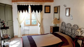 A bedroom with a bed, a window with curtains, a bedside table with a lamp, and a chair.