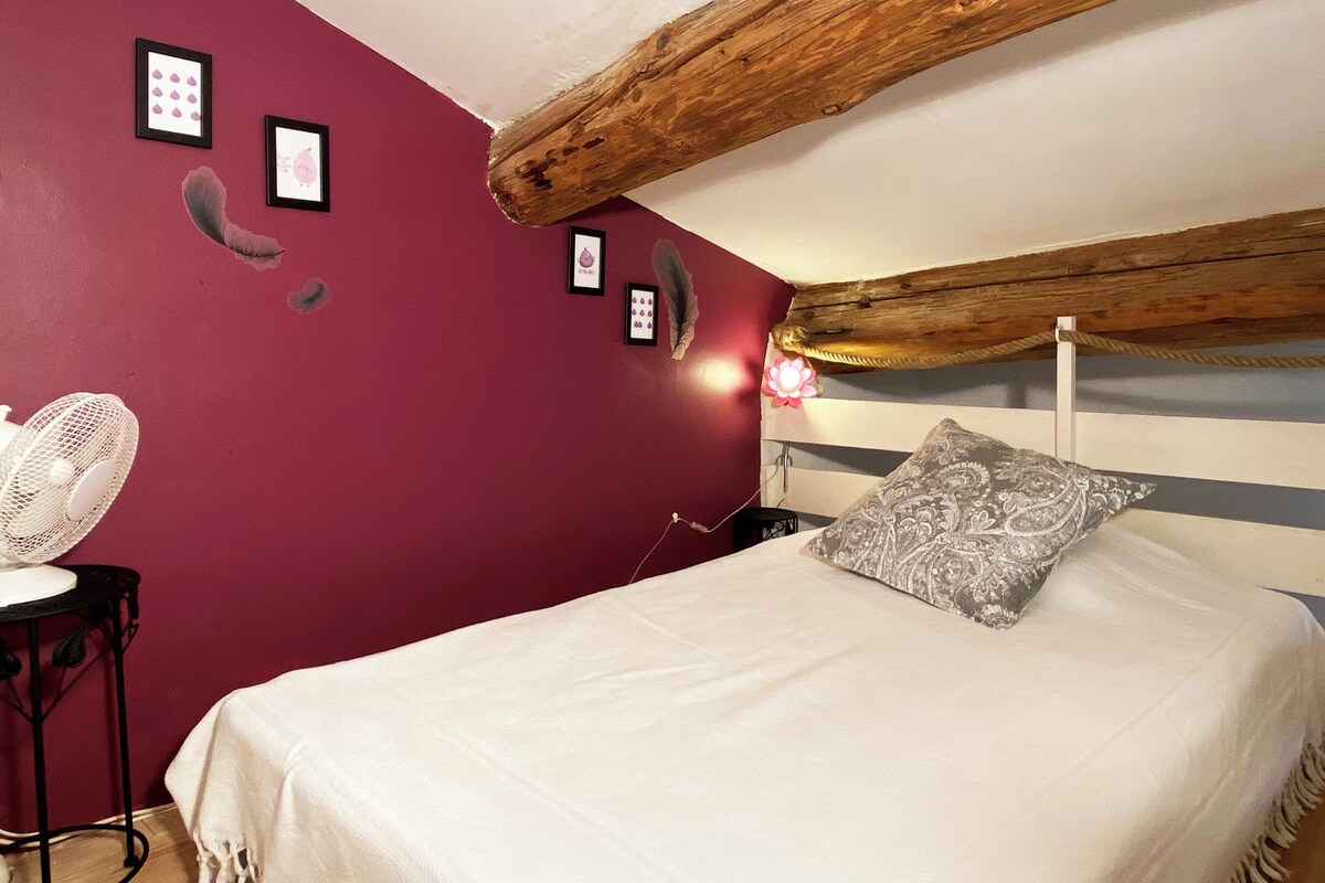 A bedroom with a red wall, a white bed, a wooden ceiling beam, and a bedside table with a lamp.