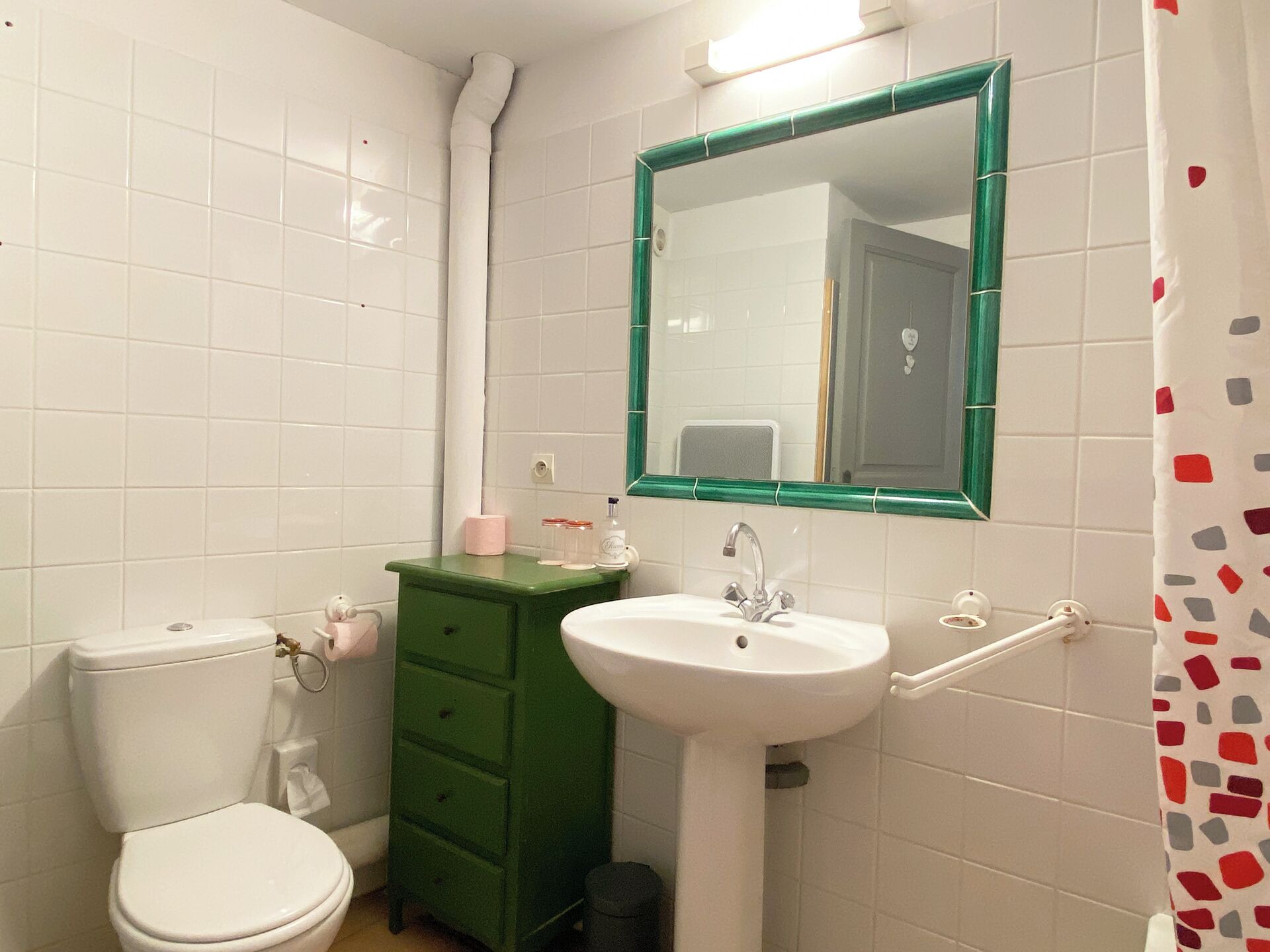 A bathroom with white tiled walls, a green vanity, a white sink, and a toilet.