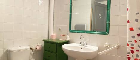 A bathroom with white tiled walls, a green vanity, a white sink, and a toilet.