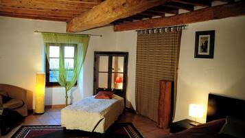 Ein gemütliches Zimmer mit Bett, Sessel, Tisch und Lampe. Ein Fenster mit Vorhängen und eine Tür mit Spiegel.