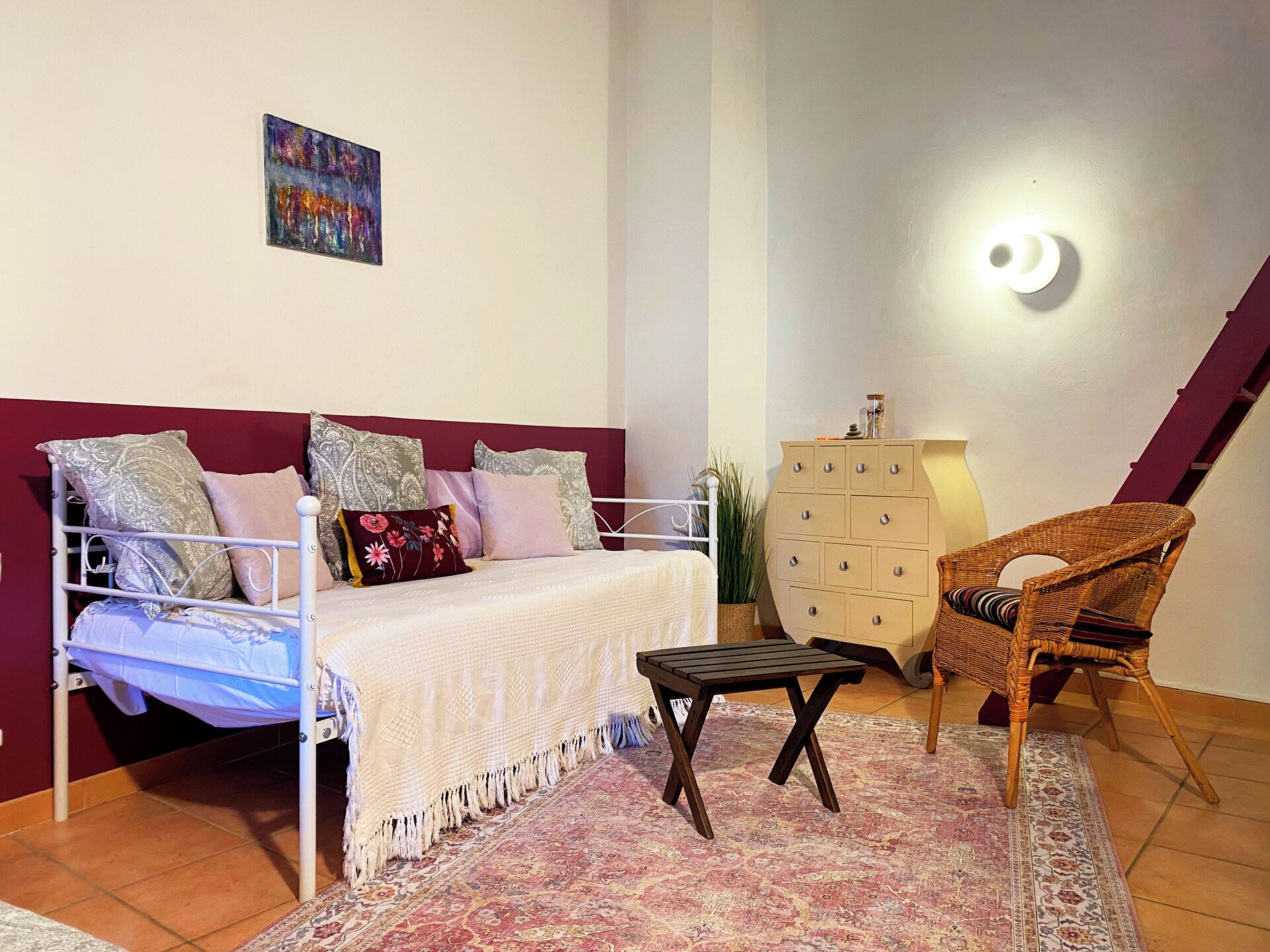 Une chambre à coucher comprenant un lit, une commode, une chaise, un tapis et un luminaire fixé au mur.