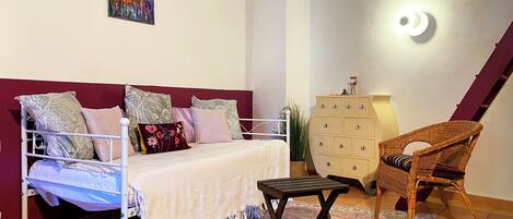 Une chambre à coucher comprenant un lit, une commode, une chaise, un tapis et un luminaire fixé au mur.