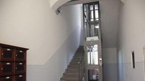 A staircase with a glass elevator door, a wooden cabinet with multiple compartments, and a plain wall. - Testaccio Piramide by Interhome (Rome: Historical City Center)