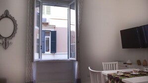 A room with a dining table, chairs, a television, and a window with curtains. - Testaccio Piramide by Interhome (Rome: Historical City Center)