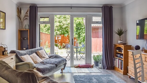A living room with a sofa, a coffee table, a bookshelf, and a TV. There is a sliding glass door leading to a patio with a table and chairs. - 2 bedroom accommodation in Wareham (Wareham)