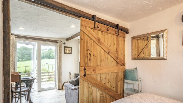 Een slaapkamer met een grote houten deur, een bed, een raam en uitzicht op een tuin.