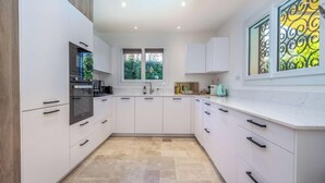 Een moderne keuken met witte kasten, een ingebouwde oven en een raam met decoratieve ijzeren omlijsting.