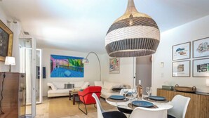Een moderne woonkamer met een eethoek, een groot schilderij en een bijzondere kroonluchter.