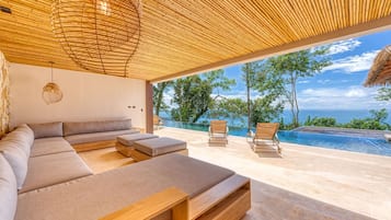 Un espace de vie extérieur moderne, doté d’une piscine, de meubles en bois et offrant une vue sur l’océan.