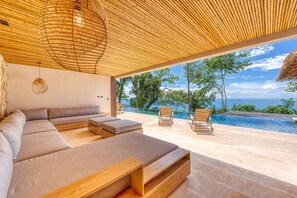 A modern outdoor living area with a pool, wooden furniture, and a view of the ocean. - ABSOLUTE luxury design mansion SECURITY - Yoga Shala - Concierge Services (Uvita)