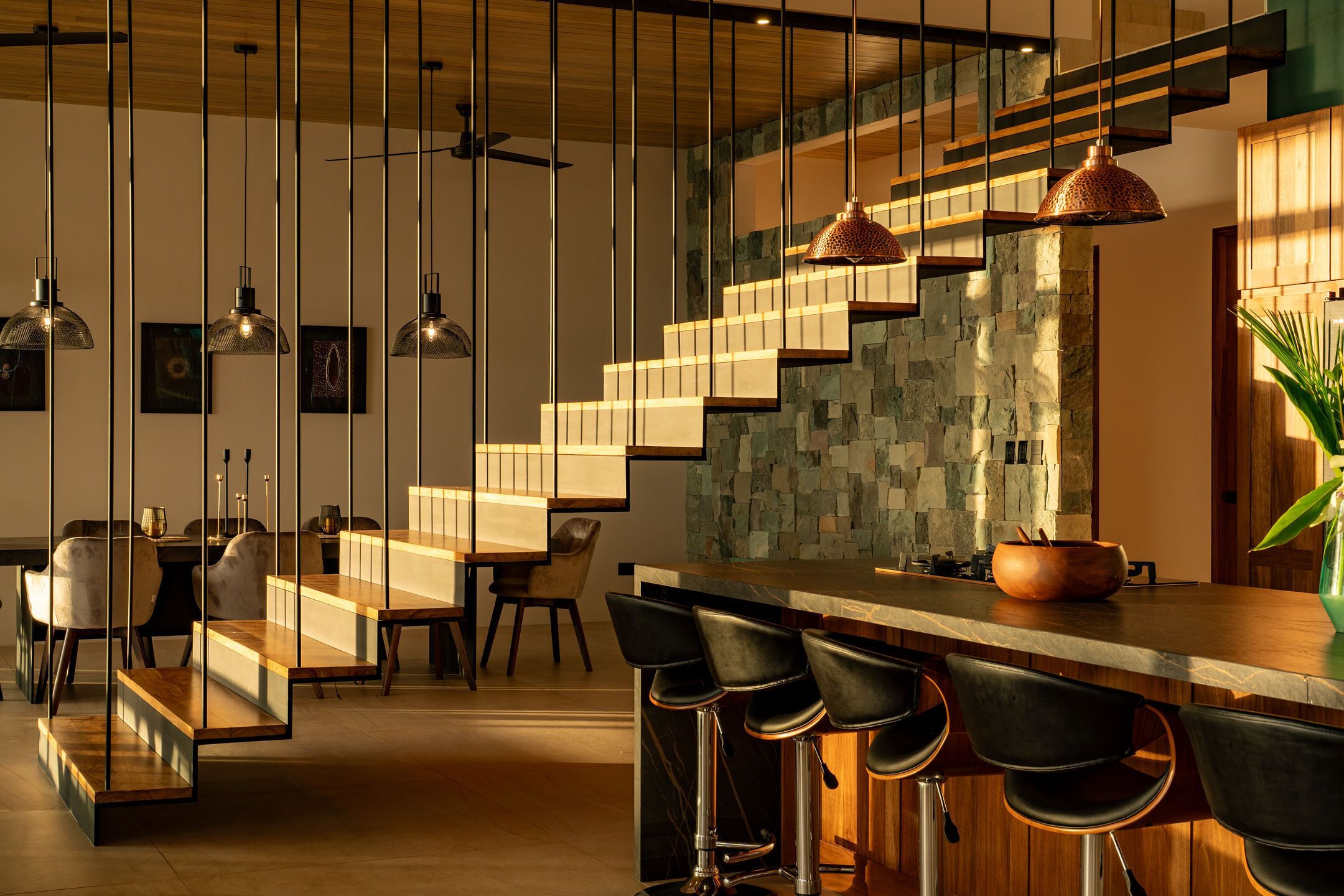 Une cuisine moderne avec un mur arrière en pierre, des tabourets de bar en bois et des luminaires suspendus.