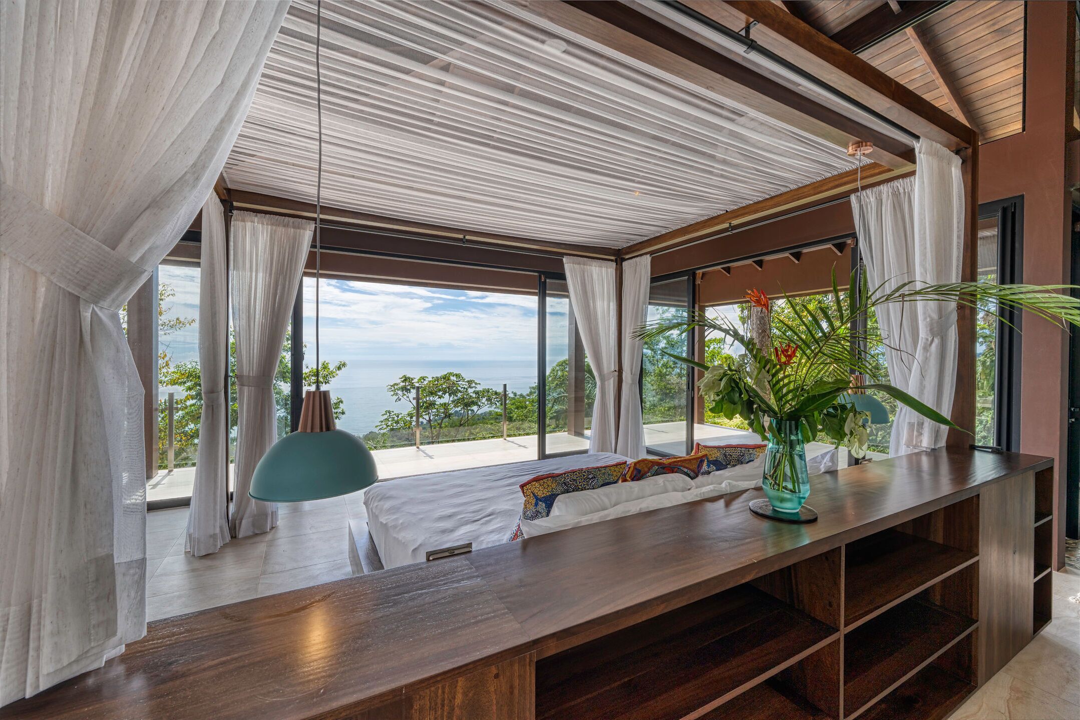 Une chambre à coucher moderne avec une grande fenêtre, une table de chevet en bois et une vue sur l’extérieur.