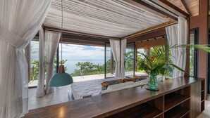 Ein modernes Schlafzimmer mit großem Fenster, einem Nachttisch aus Holz und Blick ins Freie.