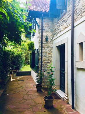 A stone-paved courtyard with potted plants, a stone wall, and a window with shutters. - authentique house, ocean first line, private access to the beach (guéthary)