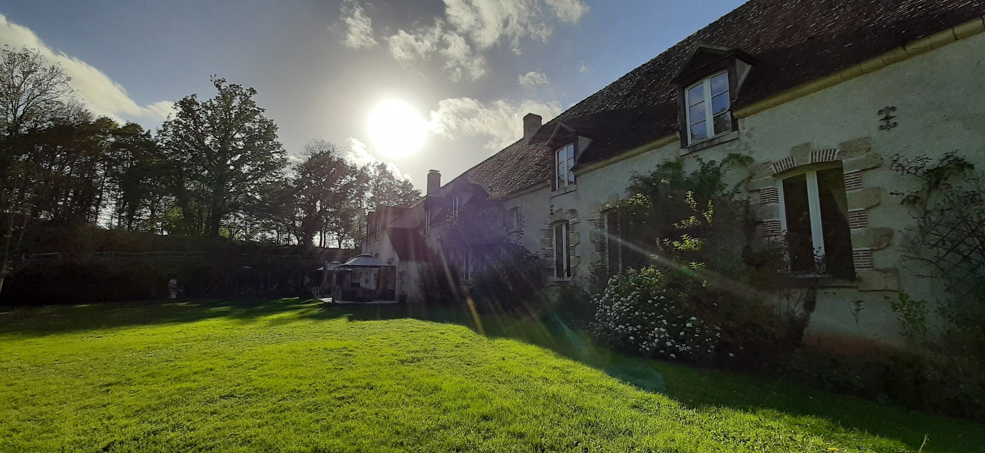 Un bâtiment doté d’un toit en pente, d’un petit jardin et d’un ciel dégagé où le soleil brille.