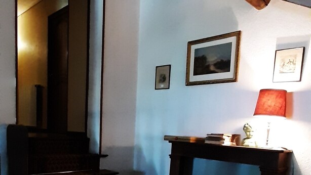 A dimly lit room with a staircase leading to a dark upper level. There is a small table with a lamp and a framed picture on the wall. - Magnifique Domaine de Caractère en Pleine Nature (GY LES NONAINS)